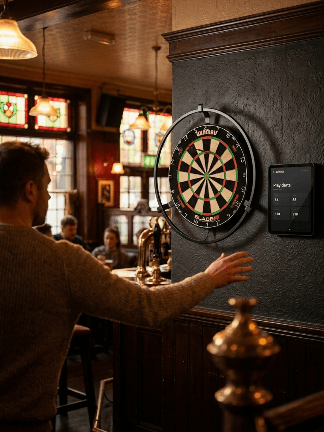Player approaching a dartboard with the SportsArena tablet mounted alongside in a British pub.